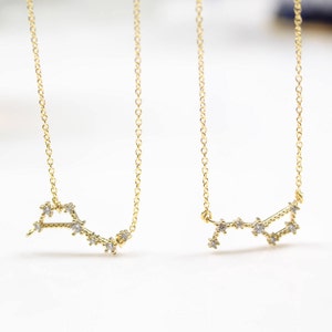 Può includere: Due collane d'oro con un designo a costellazione. Ogni collana presenta una catena delicata e un ciondolo a forma di costellazione con piccoli pietre chiare.