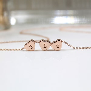 May include: A rose gold necklace featuring three heart-shaped pendants, each with a single initial. The delicate chain connects the hearts, creating a personalized and elegant piece of jewelry. The initials are "J", "L", and "S".