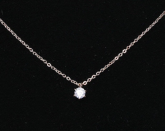 May include: A delicate gold chain necklace with a single, clear, round gemstone pendant.