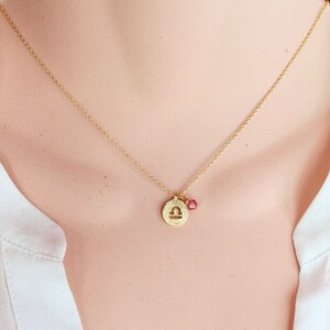 May include: Gold necklace with a Libra zodiac sign charm and a small pink gemstone.