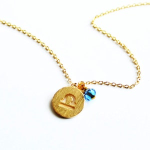 May include: Gold necklace with a Libra zodiac sign charm and blue beads.