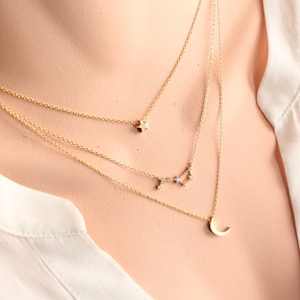 Può includere: Una collana dorata a più fili con tre ciondoli: una piccola stella, una costellazione e una luna crescente.