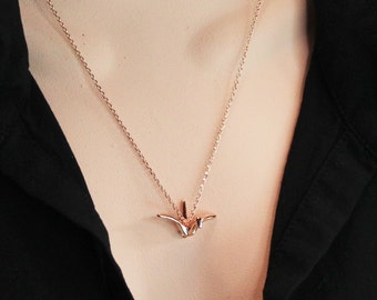 Könnte beinhalten: Eine zarte goldene Halskette mit einem kleinen Origami-Kranich-Anhänger.