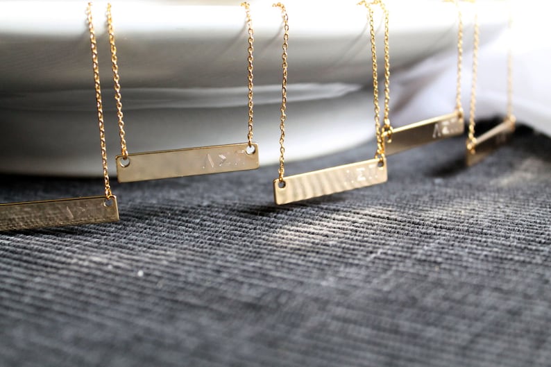 Op de afbeelding: Vijf gouden kettingen met delicate kettingen en gepersonaliseerde staafhangers. De hangers zijn rechthoekig en hebben een gehamerde textuur.