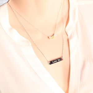 Op de afbeelding: Een zilveren ketting met een staafhanger met de tekst "Love Ya" en een kleinere ketting met drie kleine ronde bedels.
