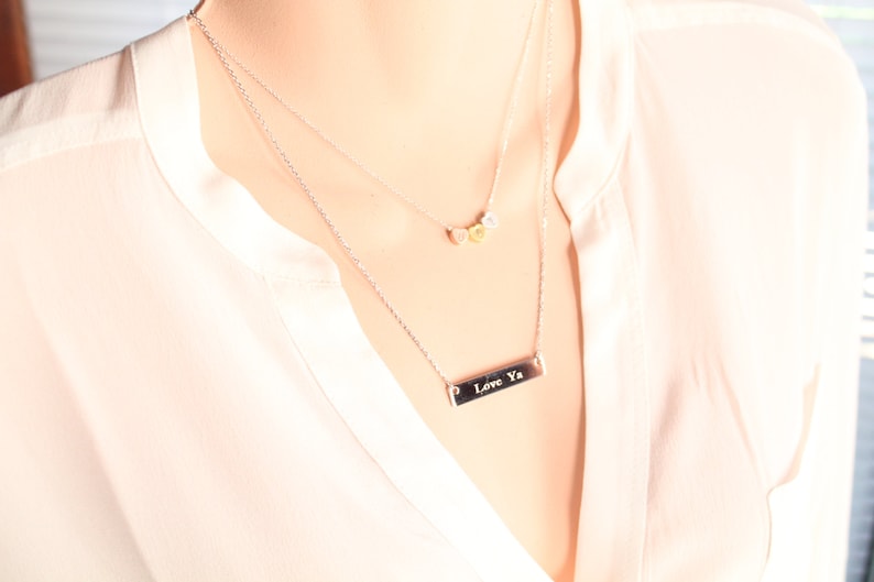Op de afbeelding: Een zilveren ketting met een staafhanger met de tekst "Love Ya" en een kleinere ketting met drie kleine ronde bedels.