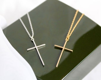 May include: Two delicate gold and silver cross necklaces on a green velvet background. The necklaces feature simple, minimalist cross pendants.