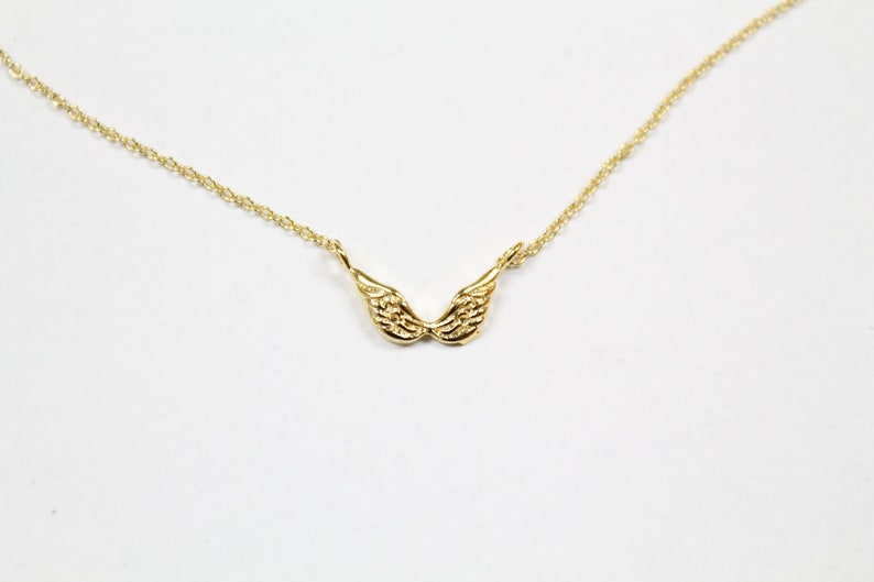 May include: A gold chain necklace with a small, detailed angel wing pendant.