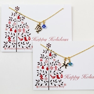 May include: Two gold necklaces with charms on white cards with a red and white Christmas tree design. The top card says "Happy Holidays" and the bottom card says "Happy Holidays".