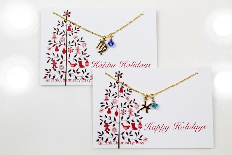 May include: Two gold necklaces with charms on white cards with a red and white Christmas tree design. The top card says "Happy Holidays" and the bottom card says "Happy Holidays".