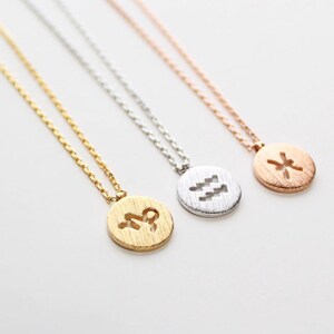 May include: Three gold, silver, and rose gold necklaces with zodiac symbols. The necklaces feature a round pendant with a cutout of the zodiac symbol. The symbols are Aquarius, Pisces, and Scorpio.