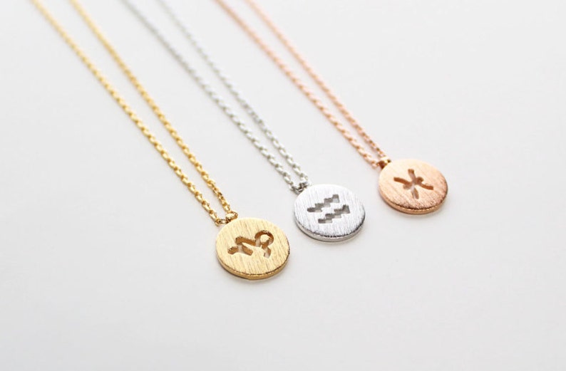 May include: Three gold, silver, and rose gold necklaces with zodiac symbols. The necklaces feature a round pendant with a cutout of the zodiac symbol. The symbols are Aquarius, Pisces, and Scorpio.
