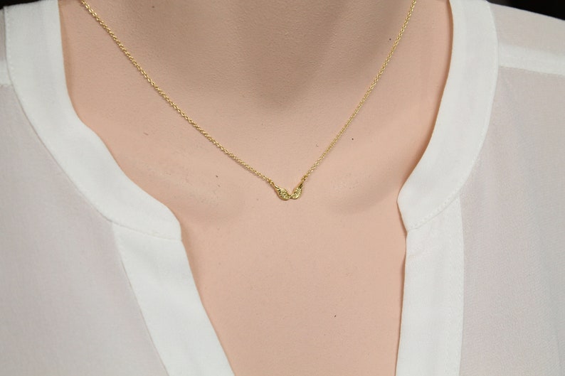 May include: A delicate gold chain necklace with a small, winged pendant.