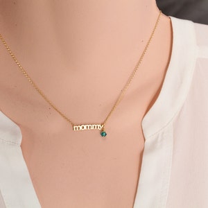 Puede incluir: Un collar de oro con un colgante de 'mam&aacute;' y un peque&ntilde;o dije de piedra azul turquesa.
