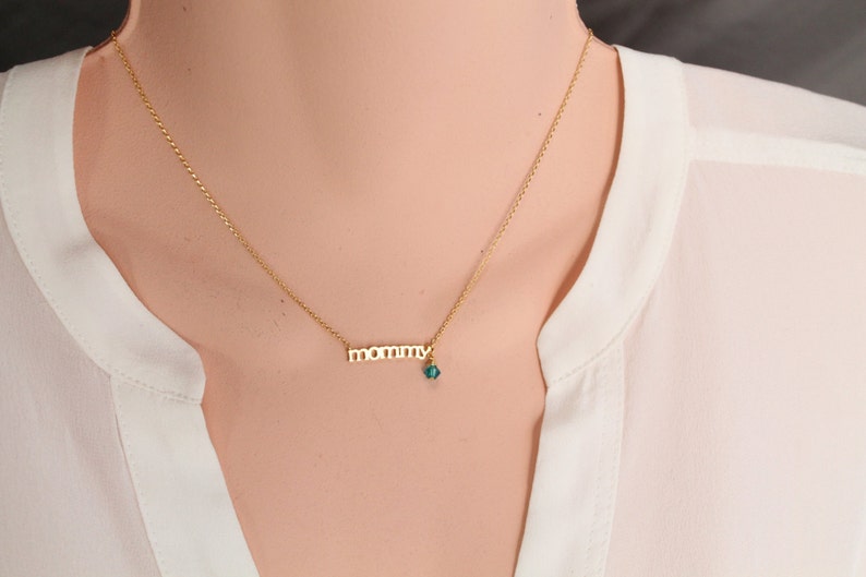 Puede incluir: Un collar de oro con un colgante de 'mam&aacute;' y un peque&ntilde;o dije de piedra azul turquesa.
