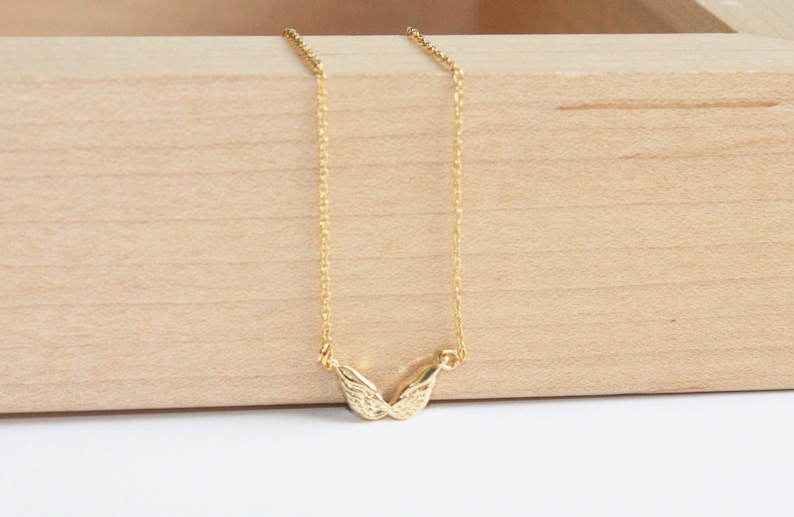 May include: A gold chain necklace with a delicate, textured, wing-shaped pendant.