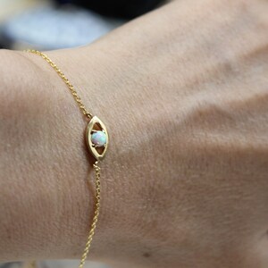 May include: A gold chain bracelet with a delicate eye charm featuring a white opal gemstone.