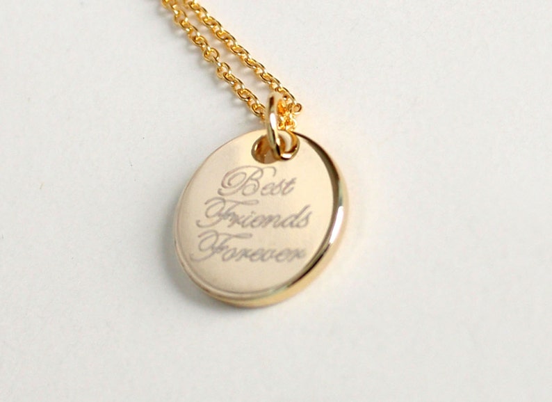 May include: Gold-colored pendant necklace with an oval charm. The charm has the words "Best Friends Forever" engraved in an elegant script. The necklace chain is also gold-colored.