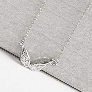 May include: A silver necklace with a delicate chain and a wing pendant. The wings are detailed and have a textured surface.