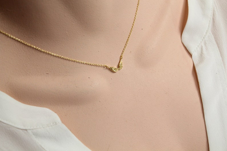 May include: A delicate gold chain necklace with a small pair of angel wings pendant.