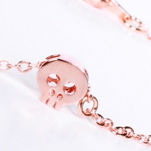 May include: A rose gold chain necklace with a small, openwork skull pendant.