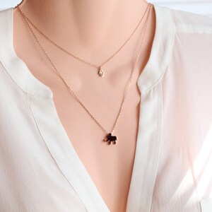 May include: A layered necklace with a small diamond pendant and a charm shaped like an elephant. The necklaces are gold-colored and worn over a white blouse.