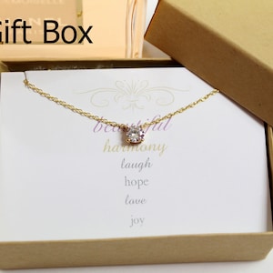 May include: A gold necklace with a small clear crystal pendant in a gift box. The box has a white card inside with the words "beautiful harmony laugh hope love joy" written on it.