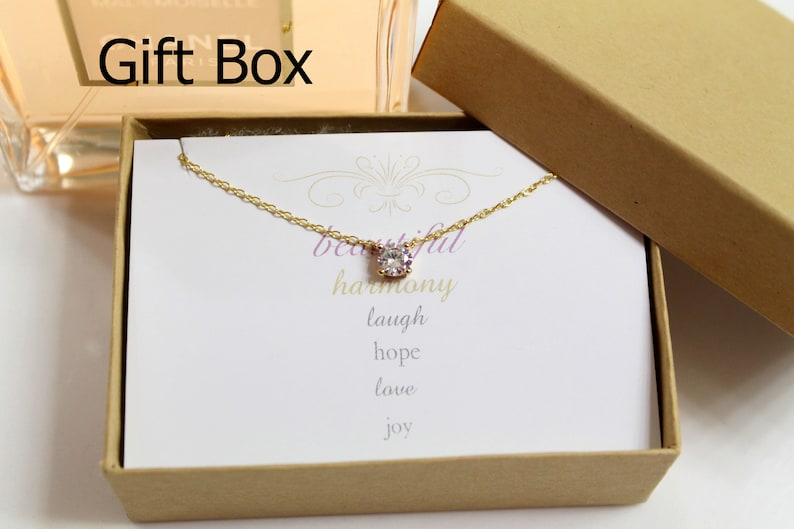 May include: A gold necklace with a small clear crystal pendant in a gift box. The box has a white card inside with the words "beautiful harmony laugh hope love joy" written on it.