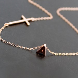 Op de afbeelding: Een delicate gouden ketting met een klein kruisbedeltje en een letter 'A' hanger.