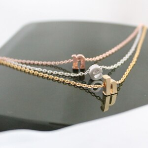 May include: Three delicate gold, silver, and rose gold chains with letter charms. The charms spell out the word "neh" in lowercase letters.