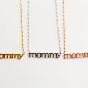 Puede incluir: Tres collares de oro con la palabra "mommy" escrita en cada uno. Los collares son de oro, plata y oro rosa.