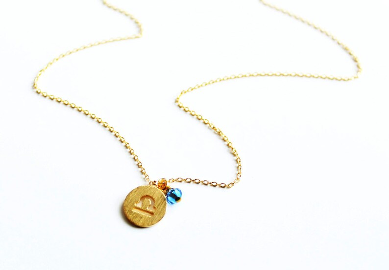 May include: Gold necklace with a Libra zodiac sign charm and blue beads.