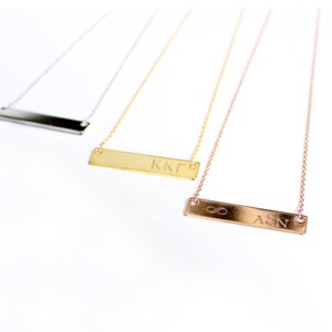 Op de afbeelding: Drie gouden bar kettingen met verschillende gravures. De bovenste ketting heeft een zilveren bar gegraveerd met "KKГ". De middelste ketting heeft een gouden bar gegraveerd met "KKГ". De onderste ketting heeft een ros&eacute;gouden bar gegraveerd met "&infin; ASN".
