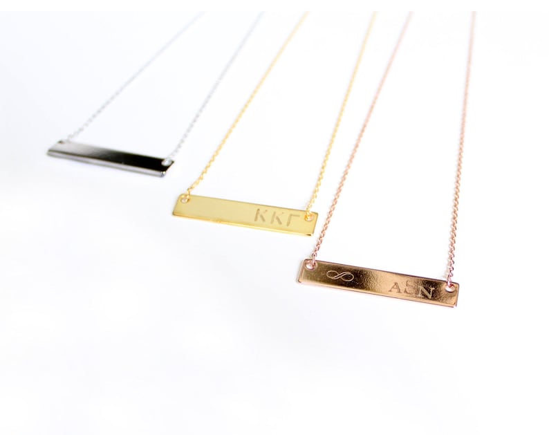 Op de afbeelding: Drie gouden bar kettingen met verschillende gravures. De bovenste ketting heeft een zilveren bar gegraveerd met "KKГ". De middelste ketting heeft een gouden bar gegraveerd met "KKГ". De onderste ketting heeft een ros&eacute;gouden bar gegraveerd met "&infin; ASN".