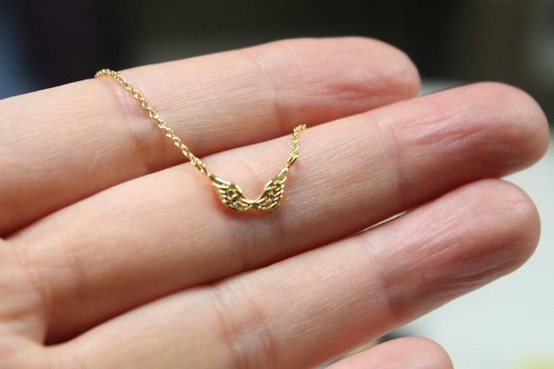 May include: A gold chain necklace with a delicate pair of angel wings pendant.