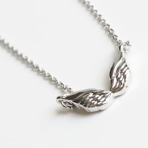 May include: Silver necklace with a delicate chain and a pair of angel wings pendant.