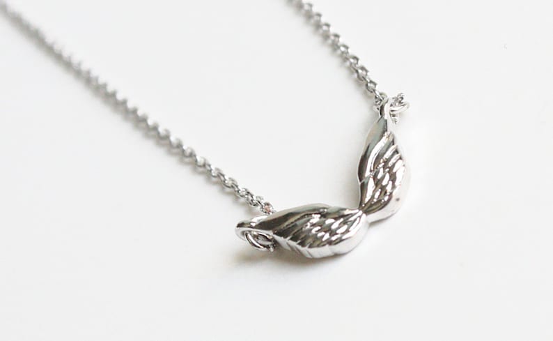 May include: Silver necklace with a delicate chain and a pair of angel wings pendant.