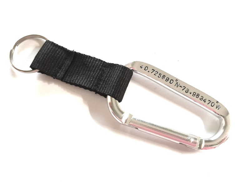 May include: Silver carabiner keychain with a black nylon strap and a key ring. The carabiner is engraved with the coordinates "40.725880&deg; N-73.983470&deg; W".