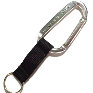 May include: A silver carabiner with a black strap and a key ring. The carabiner has the text "30.2694 N, 92.3431 W" engraved on it.