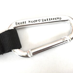 May include: A silver carabiner with a black strap attached. The carabiner is engraved with the text "Beast Mode &hearts; Buttercup".