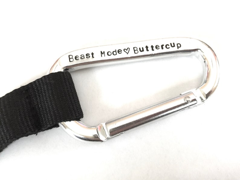 May include: A silver carabiner with a black strap attached. The carabiner is engraved with the text "Beast Mode &hearts; Buttercup".