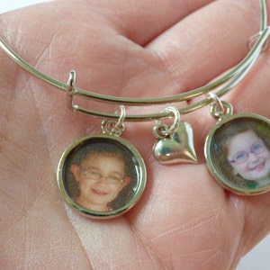 Puede incluir: Pulsera de plata con dos dijes redondos con fotos y un dije en forma de coraz&oacute;n. Los dijes con fotos muestran im&aacute;genes de ni&ntilde;os.
