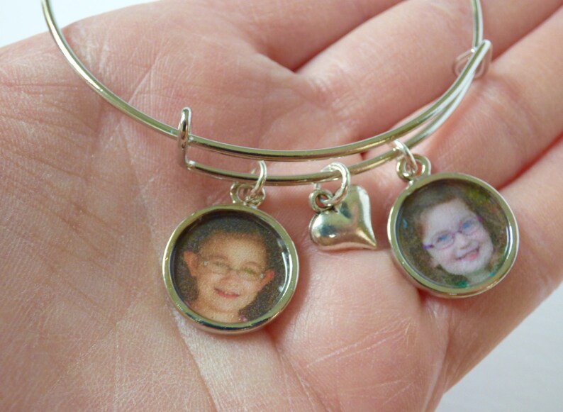 Puede incluir: Pulsera de plata con dos dijes redondos con fotos y un dije en forma de coraz&oacute;n. Los dijes con fotos muestran im&aacute;genes de ni&ntilde;os.