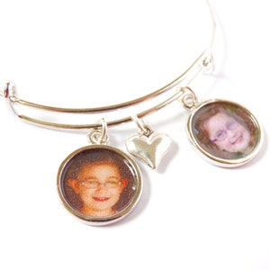 Puede incluir: Un brazalete extensible de plata con dos dijes redondos con fotos y un dije en forma de coraz&oacute;n. Los dijes con fotos muestran im&aacute;genes de primer plano de dos personas.