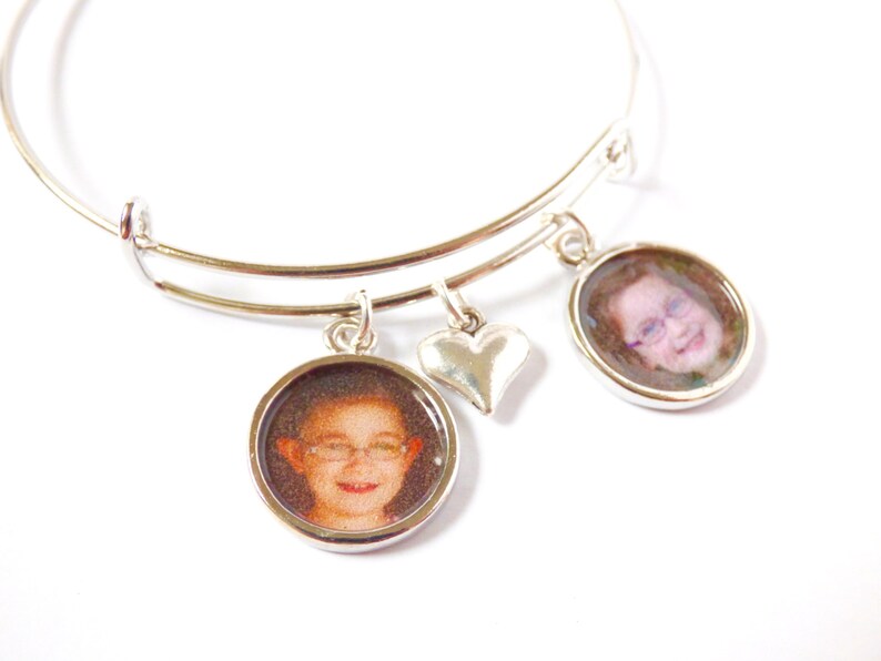 Puede incluir: Un brazalete extensible de plata con dos dijes redondos con fotos y un dije en forma de coraz&oacute;n. Los dijes con fotos muestran im&aacute;genes de primer plano de dos personas.