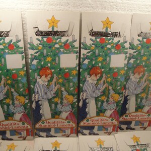 May include: Four vintage Christmas decoration boxes. Each box features a colorful illustration of a Christmas tree with ornaments and a child decorating it. The boxes have a star on top and text that reads "Qualitäts-Stanniol-Lametta."