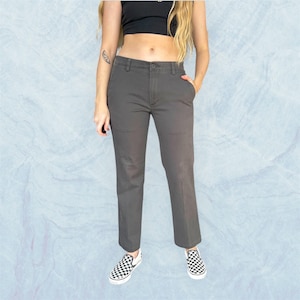 May include: Grey trousers with a button fastening and pockets. The trousers are worn with black and white chequered slip-on shoes. The person is also wearing a black crop top.