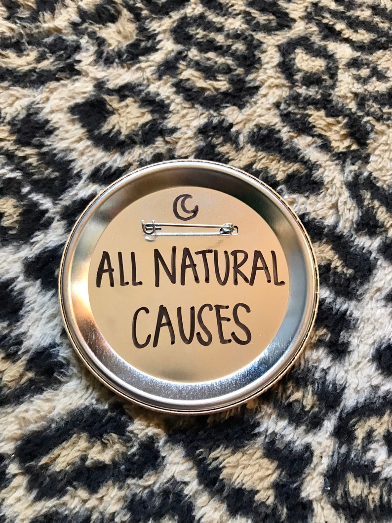May include: A silver button with the text "ALL NATURAL CAUSES" in black lettering. The button has a crescent moon design on the top.