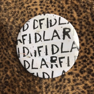 May include: White round button with the word "FIDLAR" repeated multiple times in black lettering.