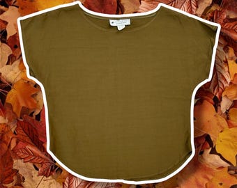 May include: A solid olive green short-sleeve top with a wide, rounded neckline and a curved hemline. The garment features a white interior neck label with black text, short cap sleeves, and a simple, unpatterned design throughout the fabric.